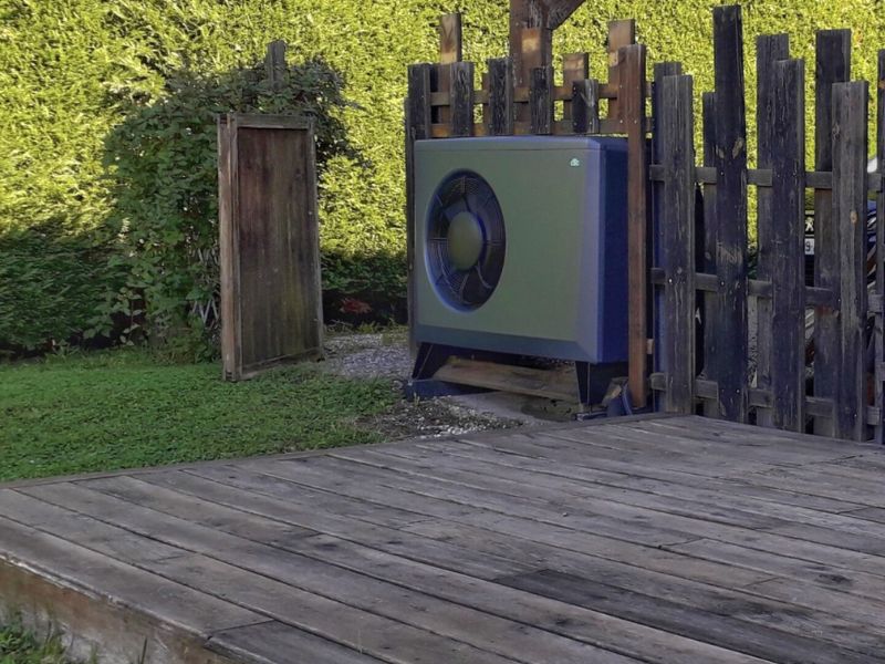 une pompe a chaleur grise installée en extérieur sur une cloture en bois avec une terrasse bois. 