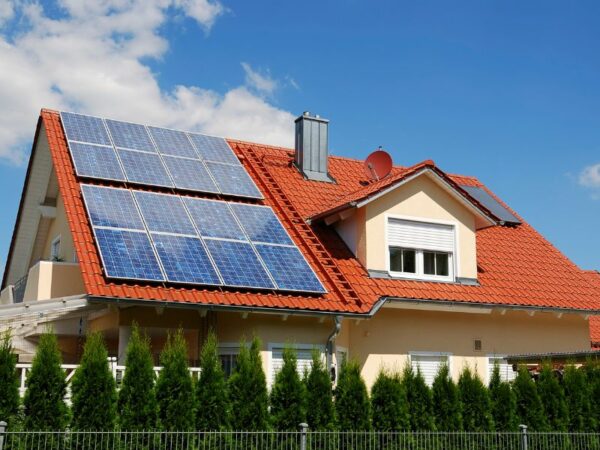 Un installateur panneaux photovoltaiques a réalisé le toit rouge de cette maison avec fenêtres et haie de cyprès.